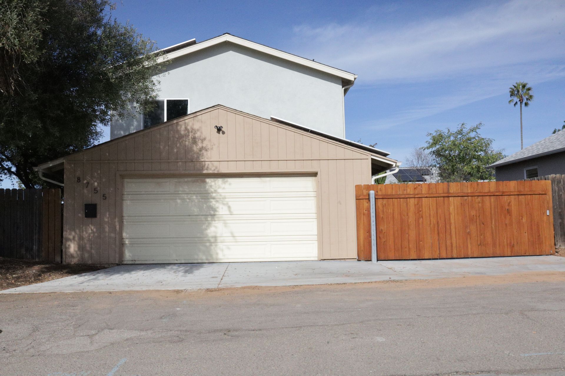 Suburban house with a white garage, tan siding, and a wooden fence on the right