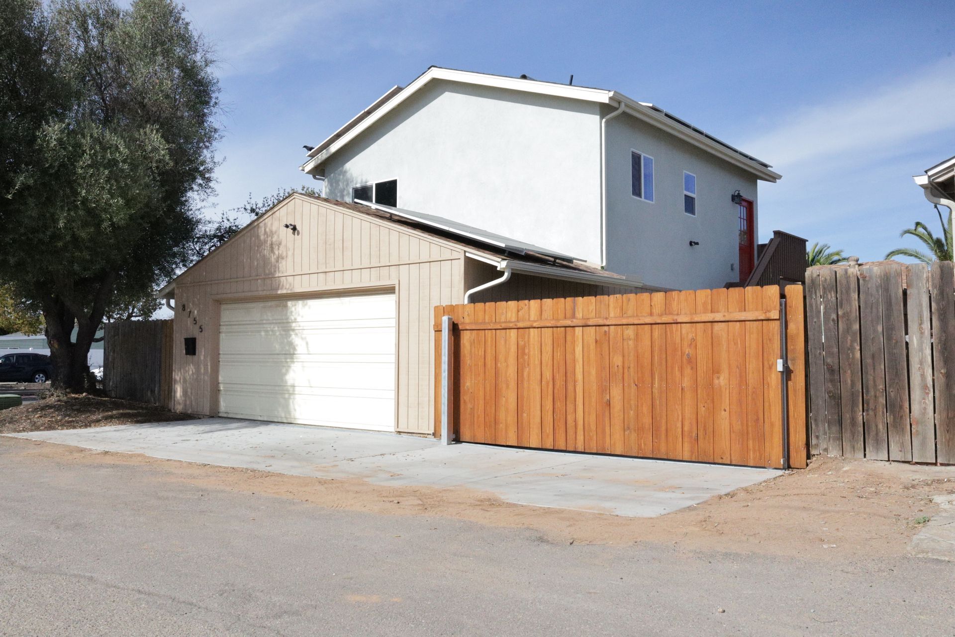 Suburban house with a white garage, tan siding, and a wooden fence along the driveway.