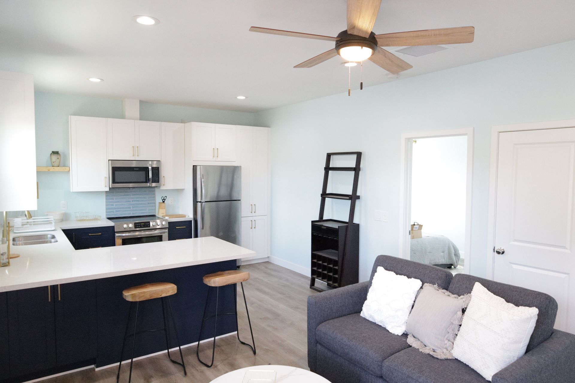 Bright modern kitchen and living room with navy island, gray sofa, ceiling fan, and stainless steel appliances