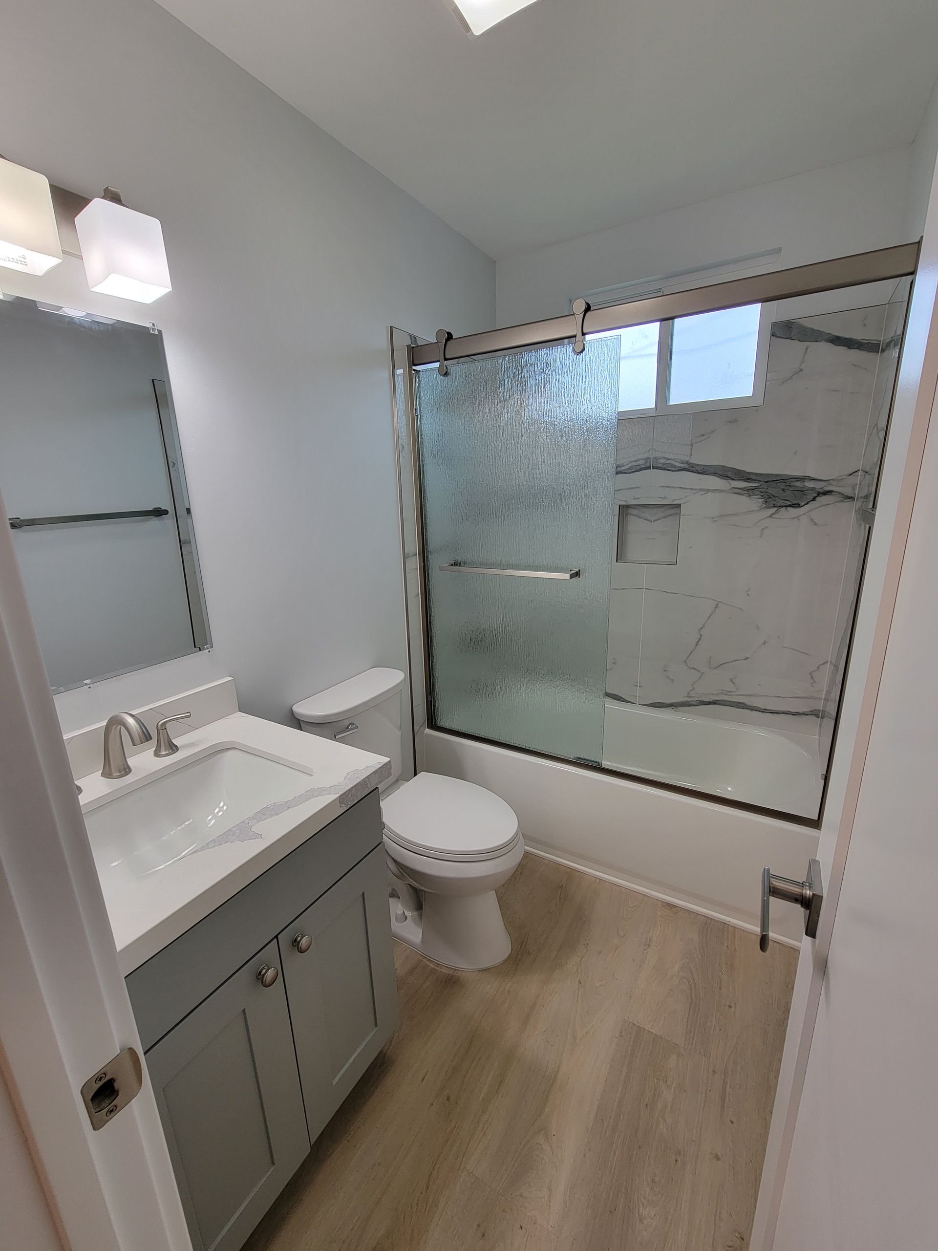 Small bathroom with gray vanity, white toilet, and frosted glass shower tub.