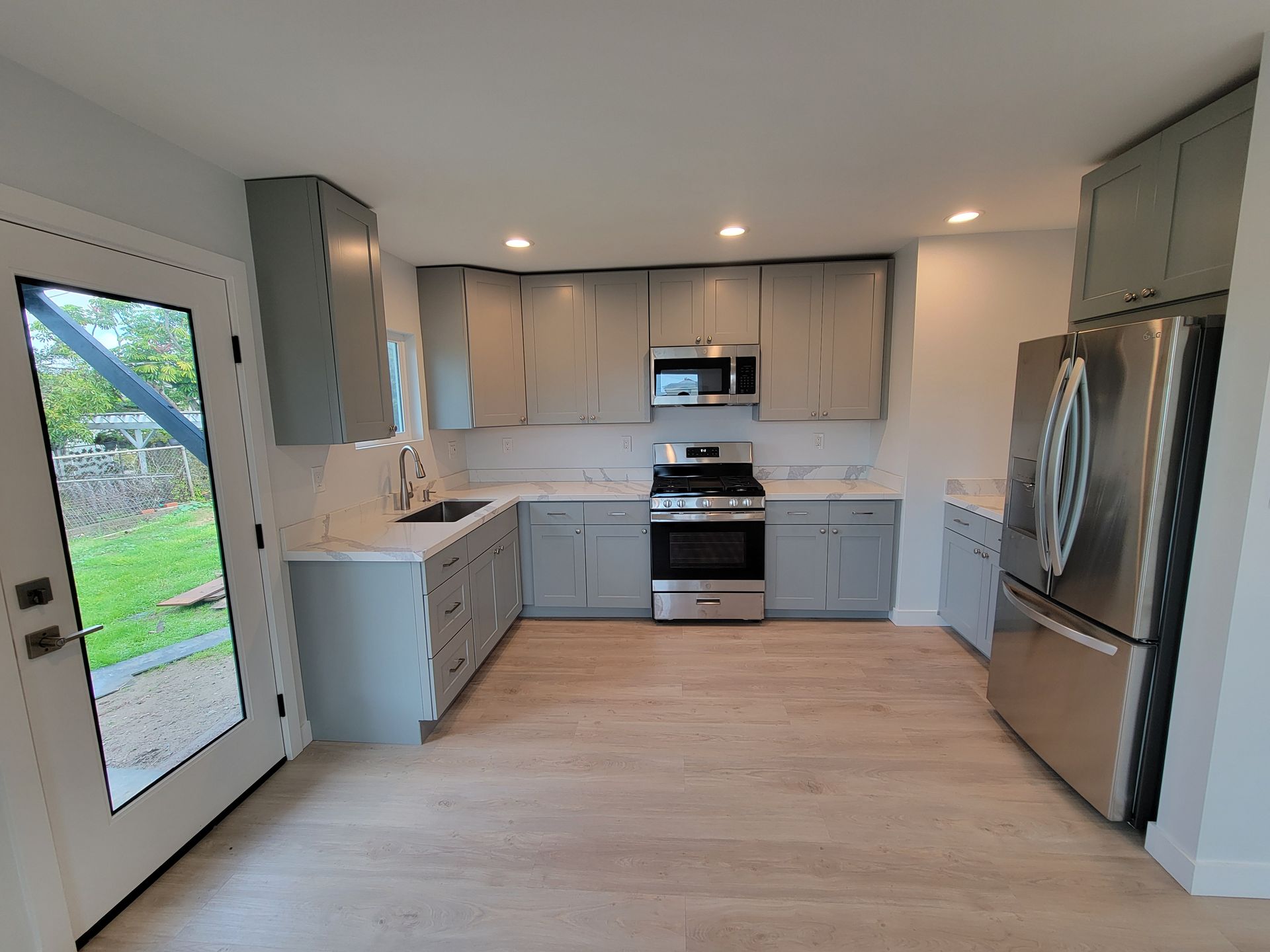 Modern kitchen with stainless steel appliances, gray cabinets, and light wood flooring.