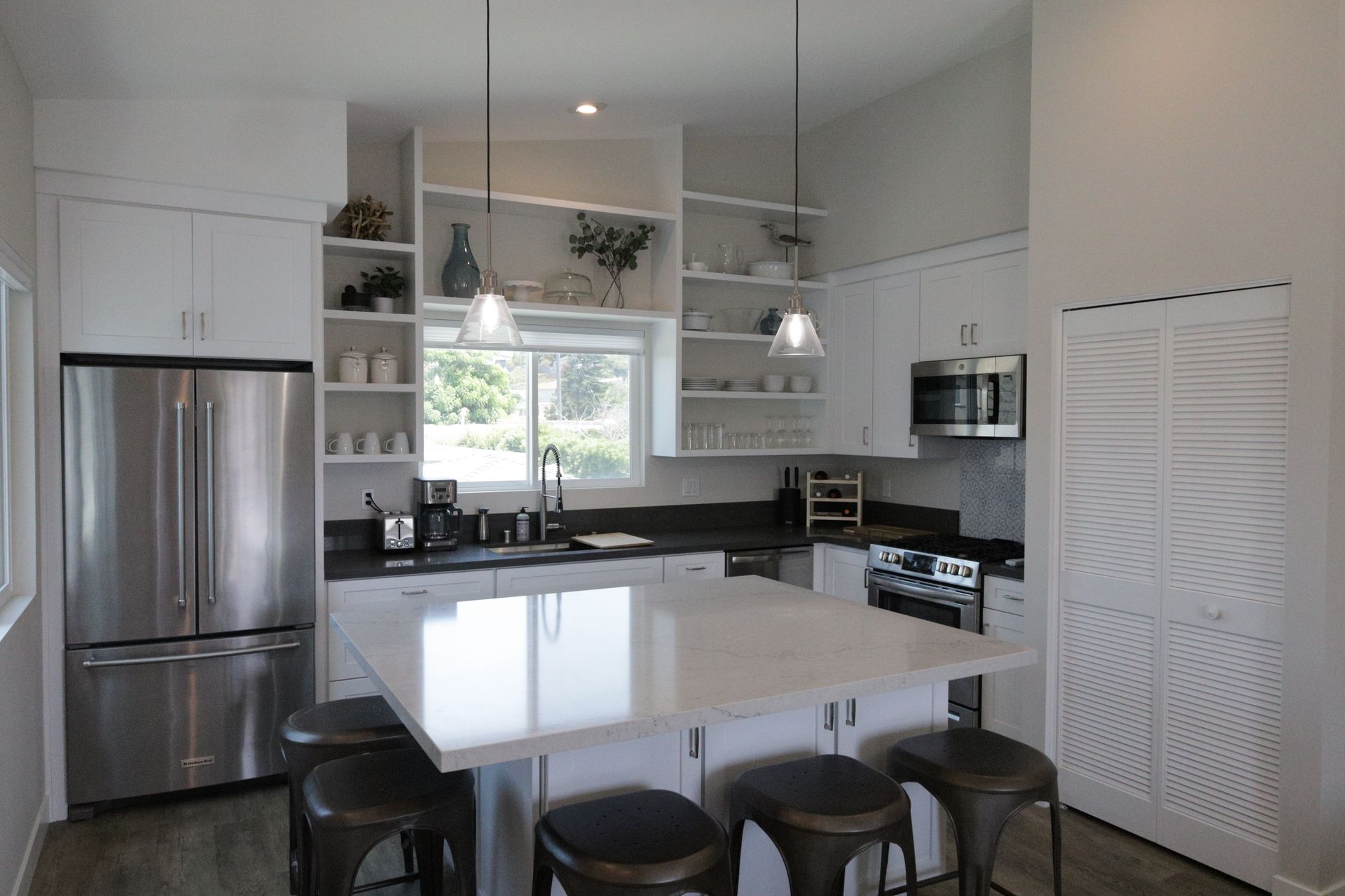 Bright modern kitchen with white island, stainless fridge, bar stools, and large window above the sink