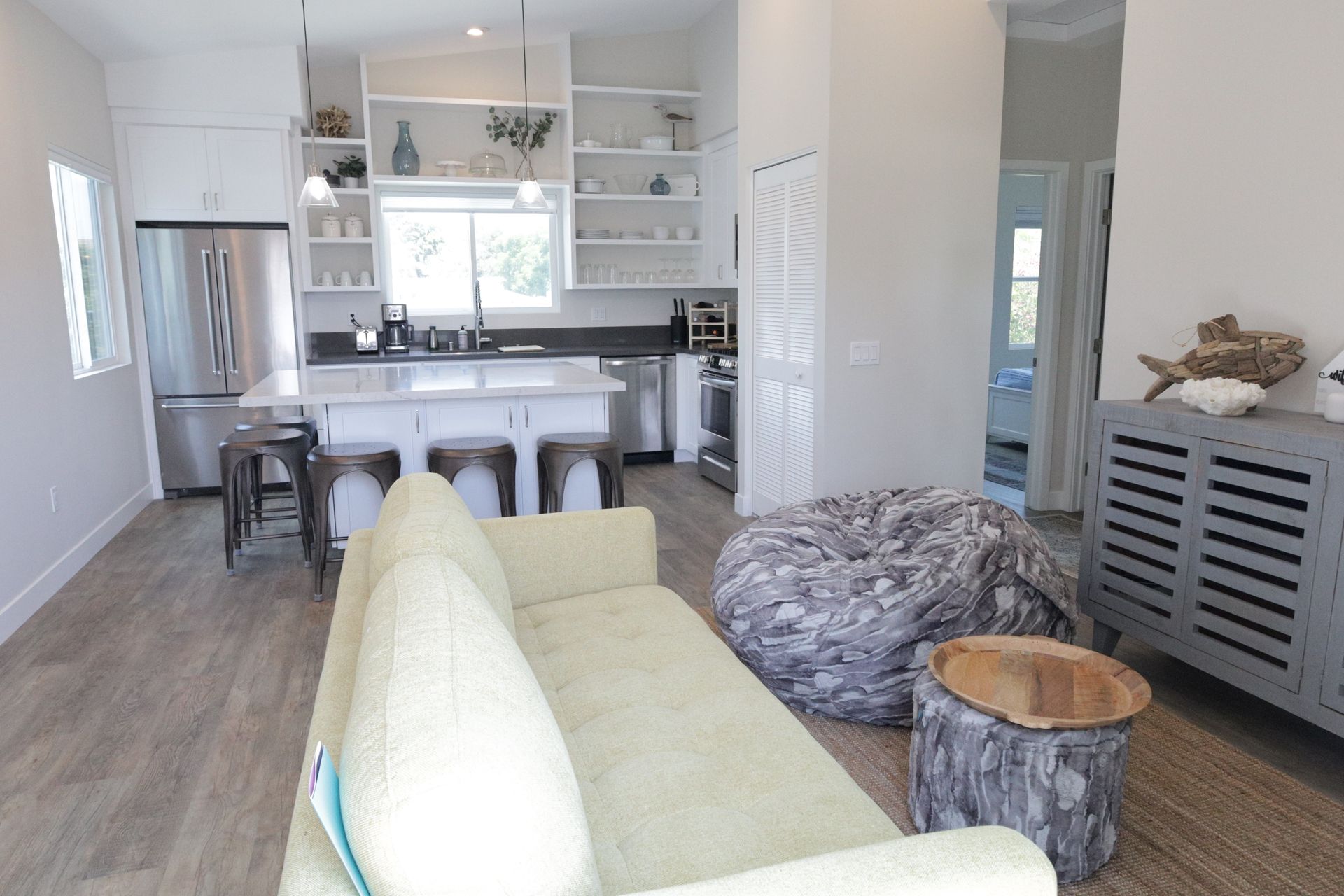 Bright open living room with pale green sofa, kitchen island, gray rug, and wood accent stools