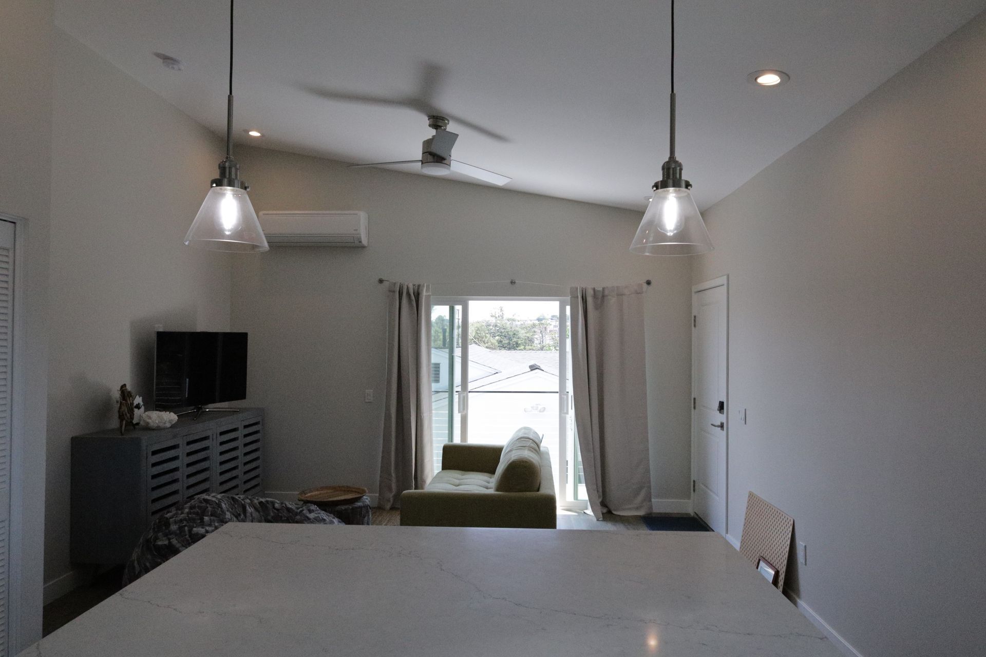 Bright living room with white walls, ceiling fan, TV, and sliding glass doors to a patio.