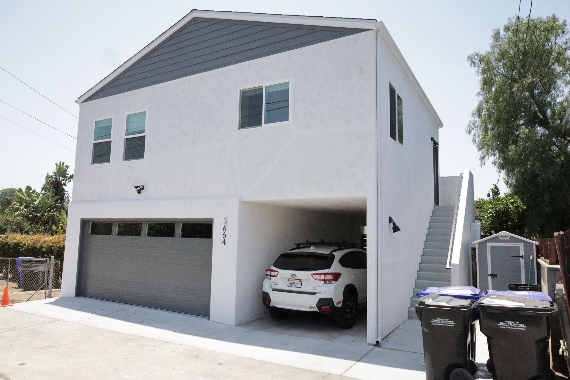 White two-story house with a garage, a car parked inside, and exterior stairs on the right.