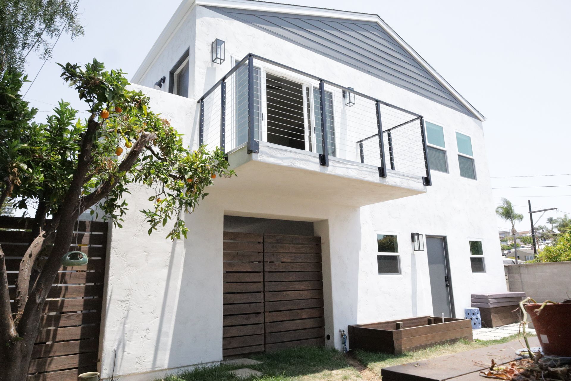 White two-story house with dark shutters, a balcony, and a tree in the front yard