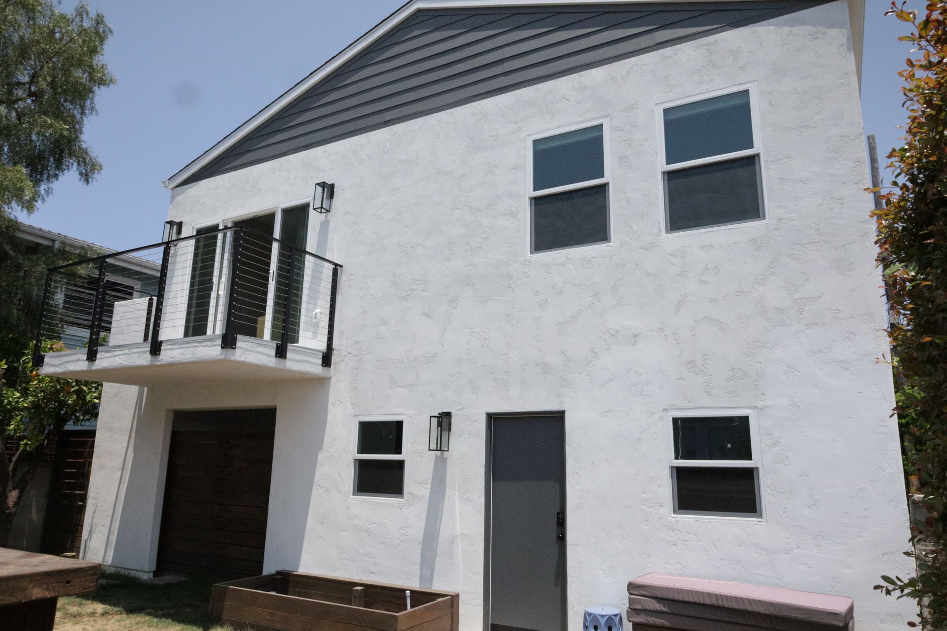Modern two-story white house with black shutters, balcony, and garage under a clear sky
