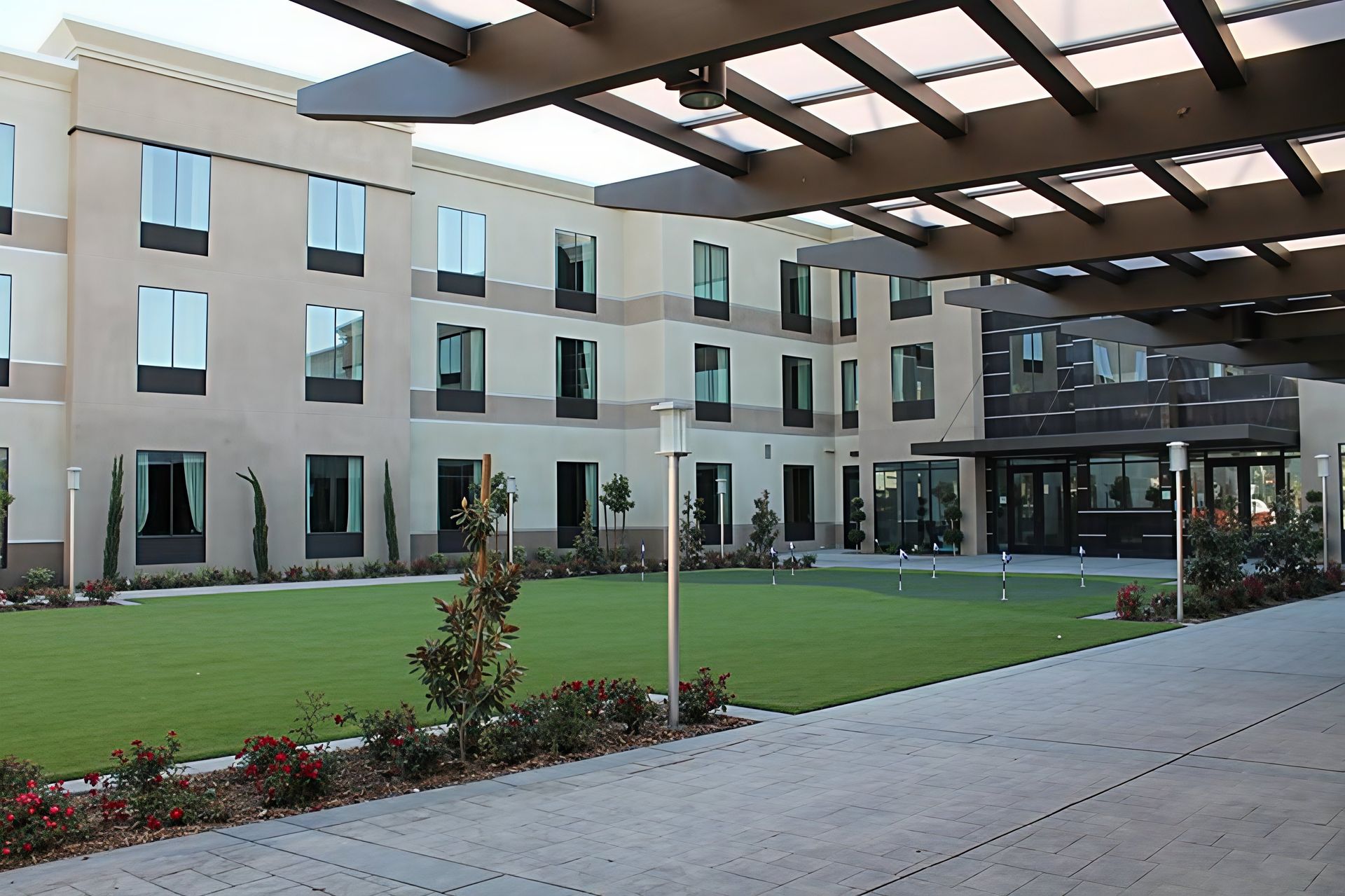 Modern apartment courtyard with green lawn, flower beds, and covered walkway between beige buildings