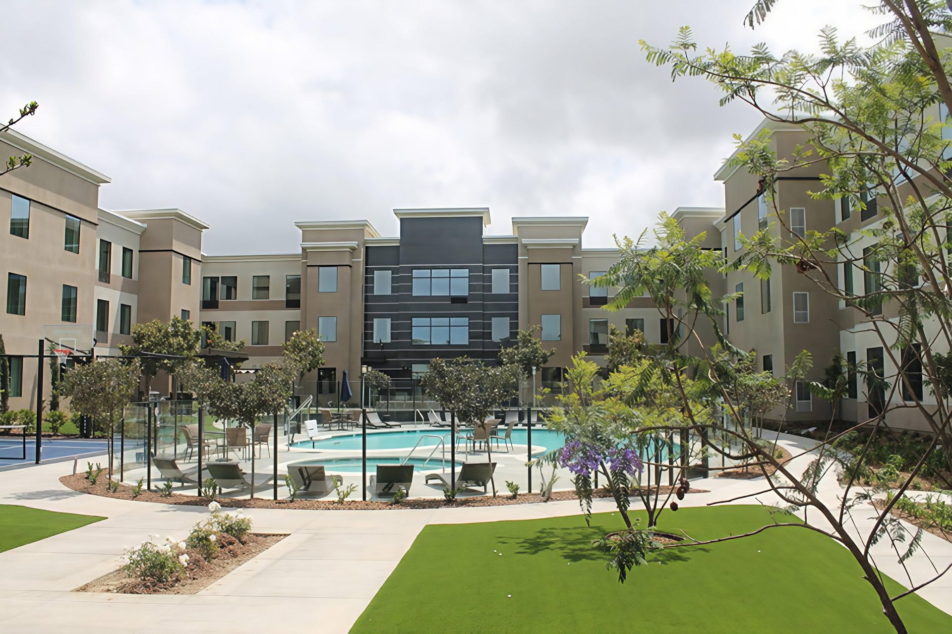 Apartment courtyard with pool, lounge chairs, and landscaped walkways under a cloudy sky