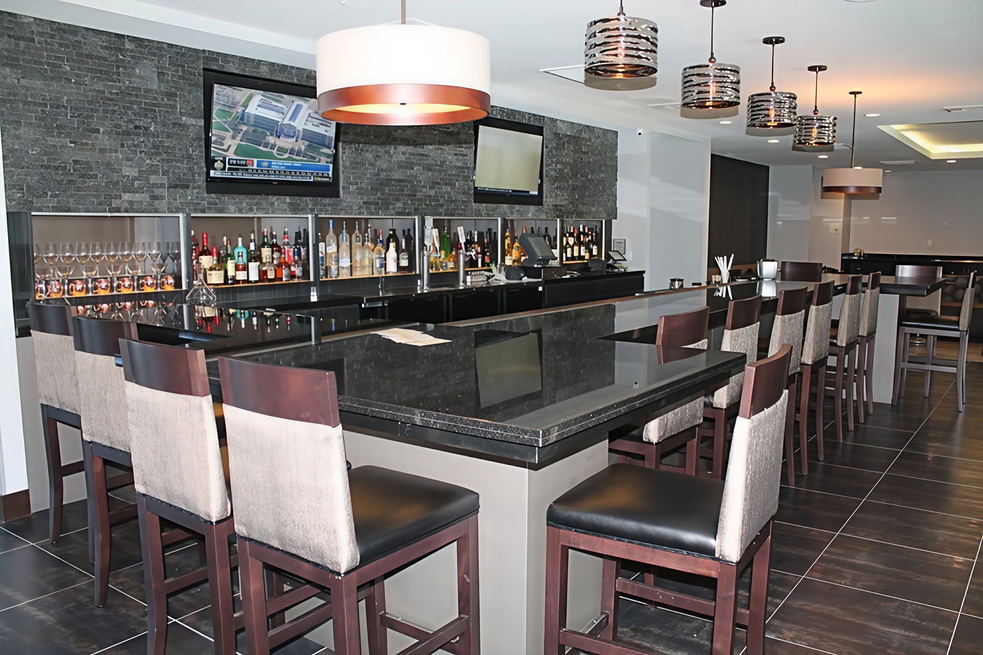 Modern bar lounge with stools, black granite counter, wall-mounted TVs, and pendant lights