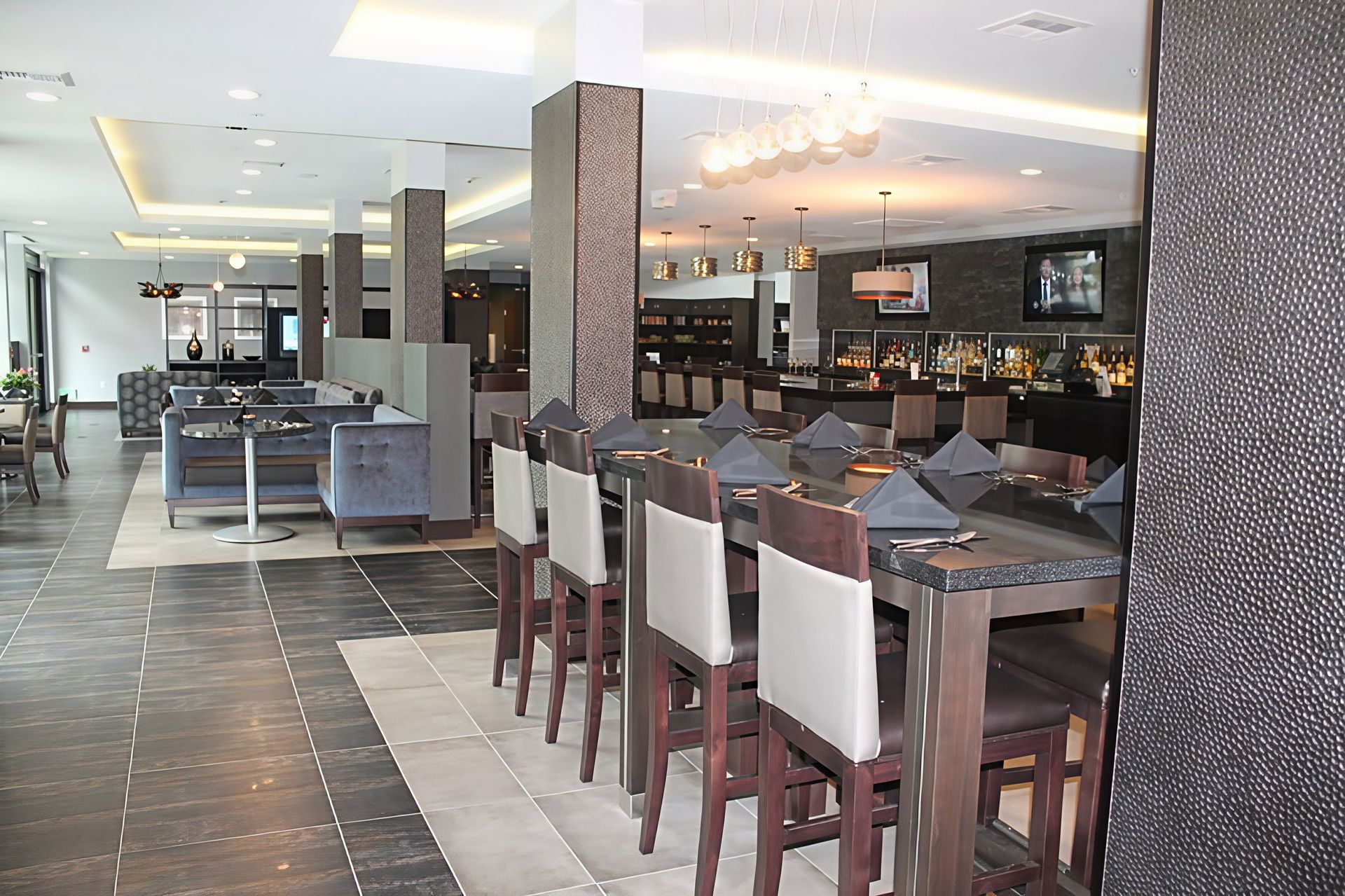 Modern restaurant dining area with bar seating, tables, and tiled floor under bright lighting