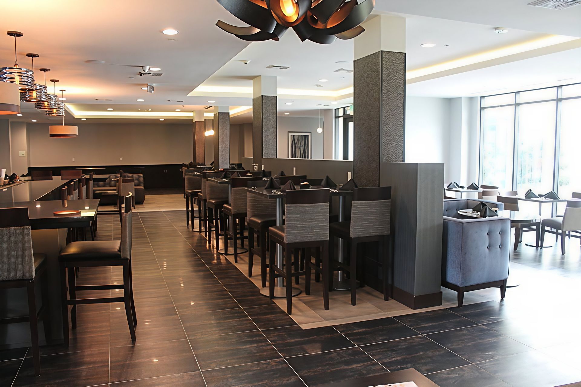 Modern restaurant interior with dark tile floor, high tables, bar stools, and large windows