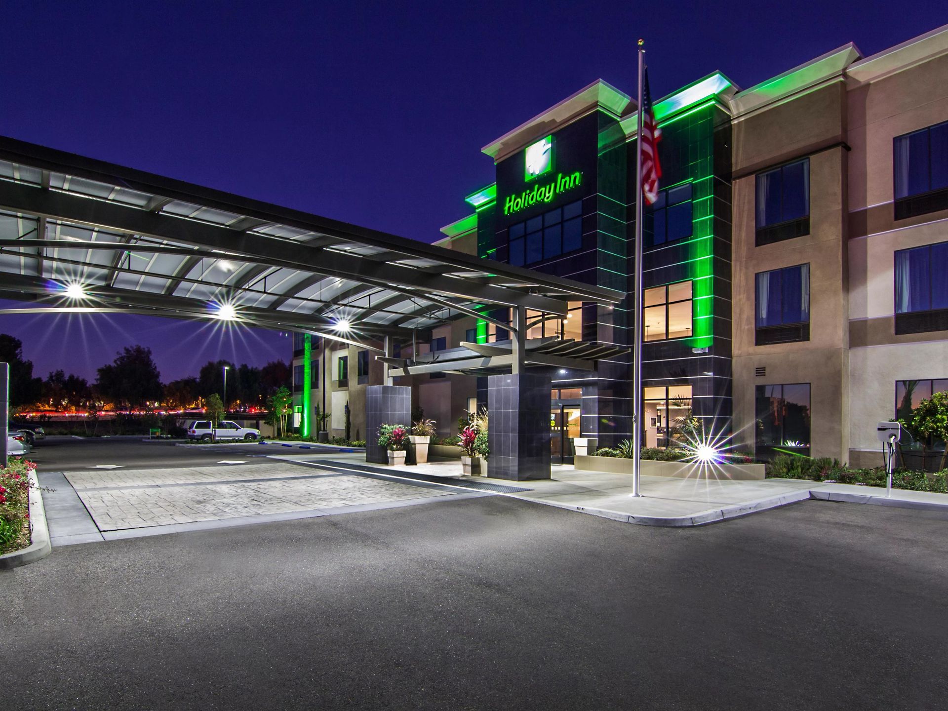 Night view of a modern hotel entrance with green-lit canopy and driveway