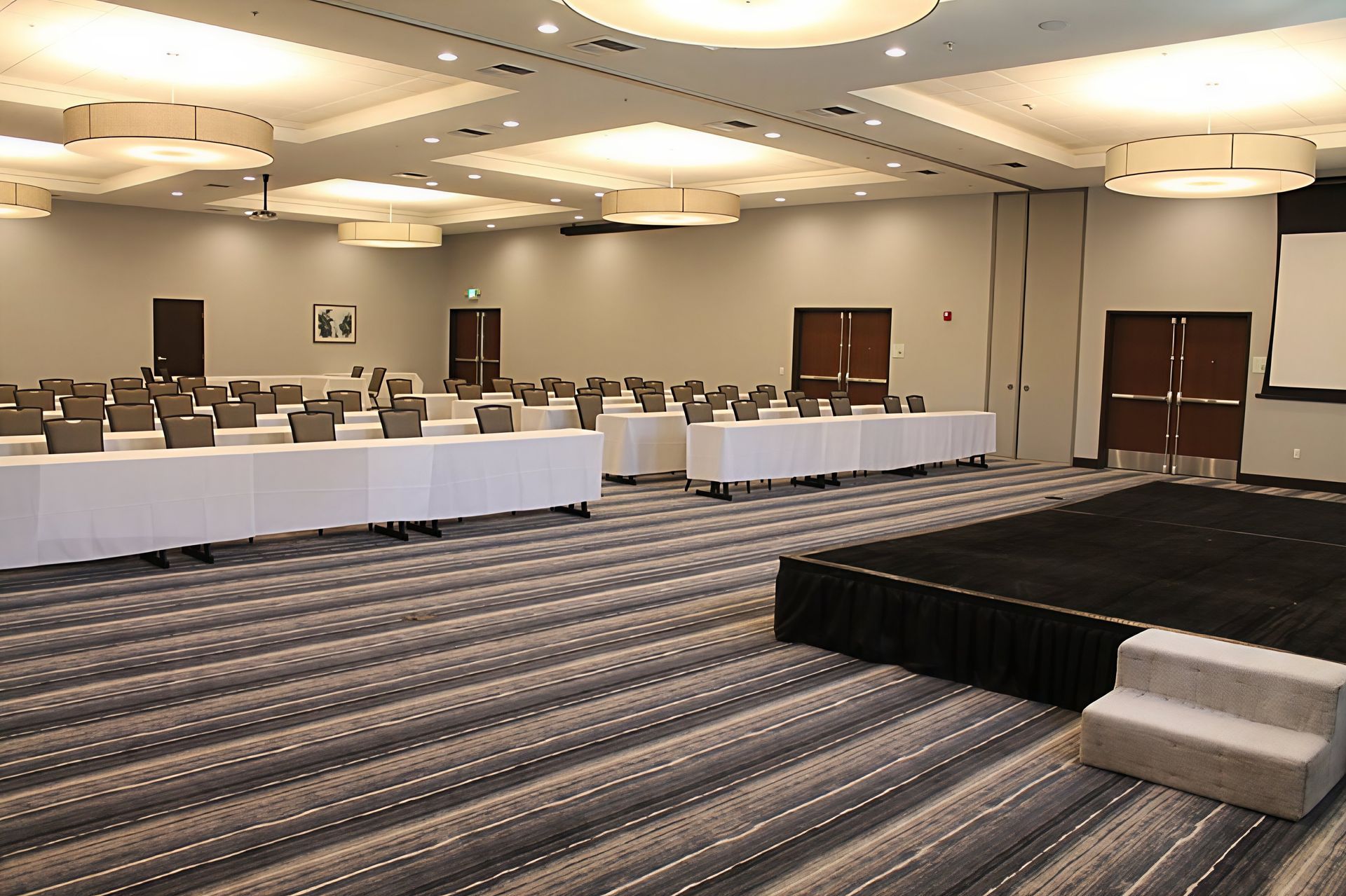 Empty conference room with tables, chairs, and a small stage on a patterned carpet.