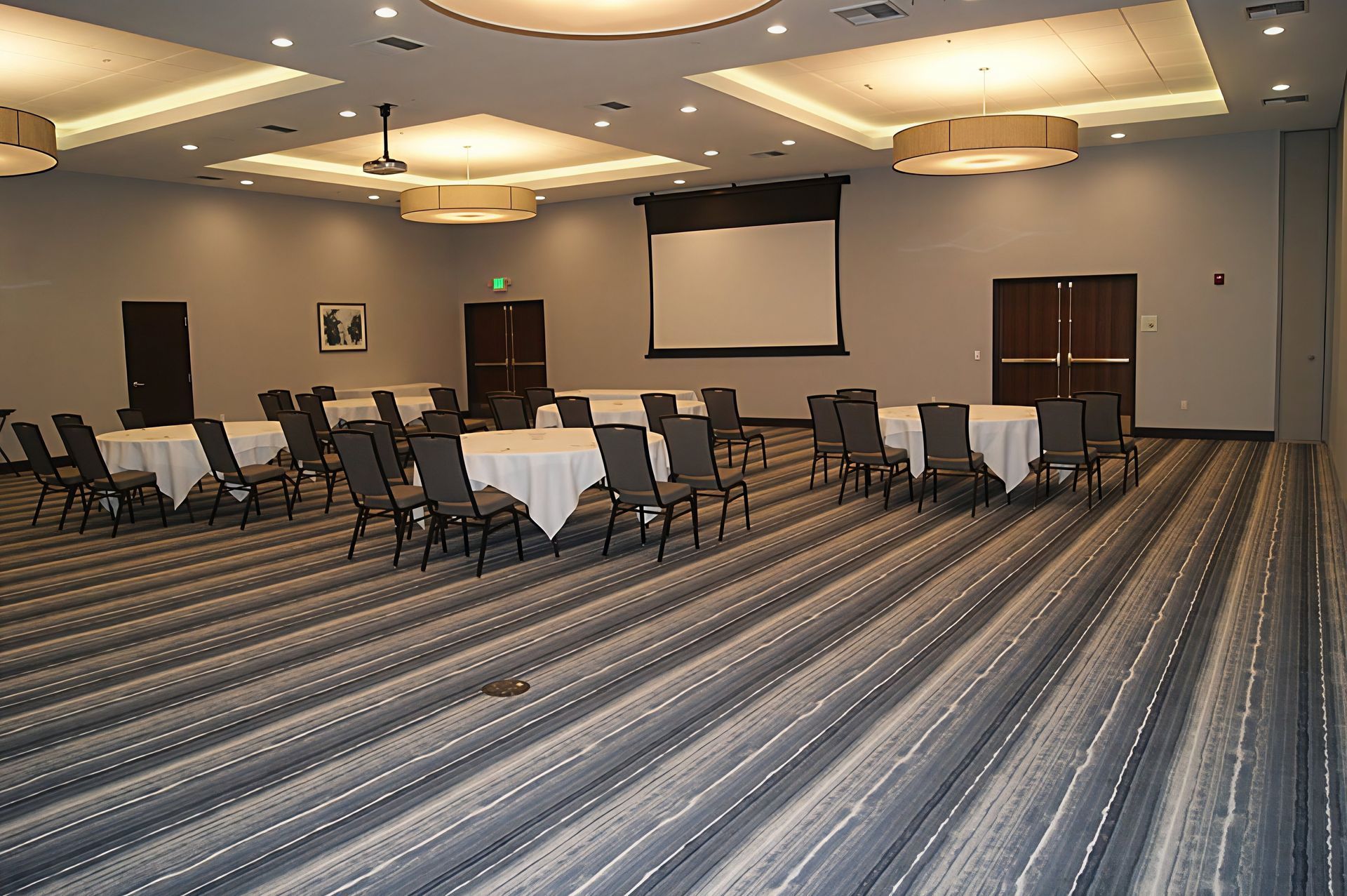 Empty conference room with rows of chairs, tables, and a projection screen on a striped carpet.