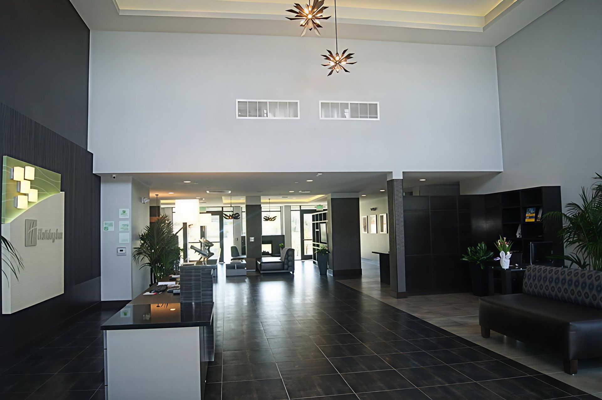 Modern hotel lobby with dark tile floor, high ceiling, seating, and glass entrance doors