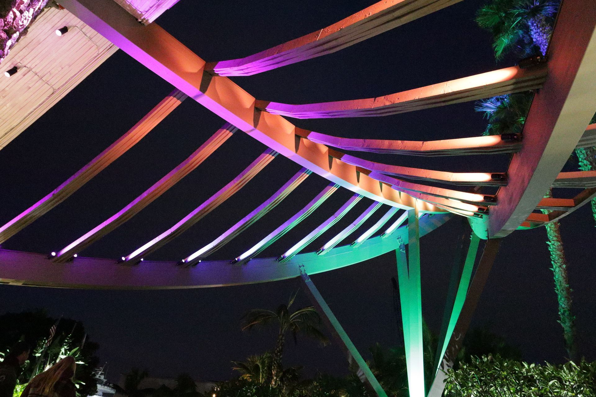 Colorful illuminated metal canopy at night with purple, pink, and green lights against the sky
