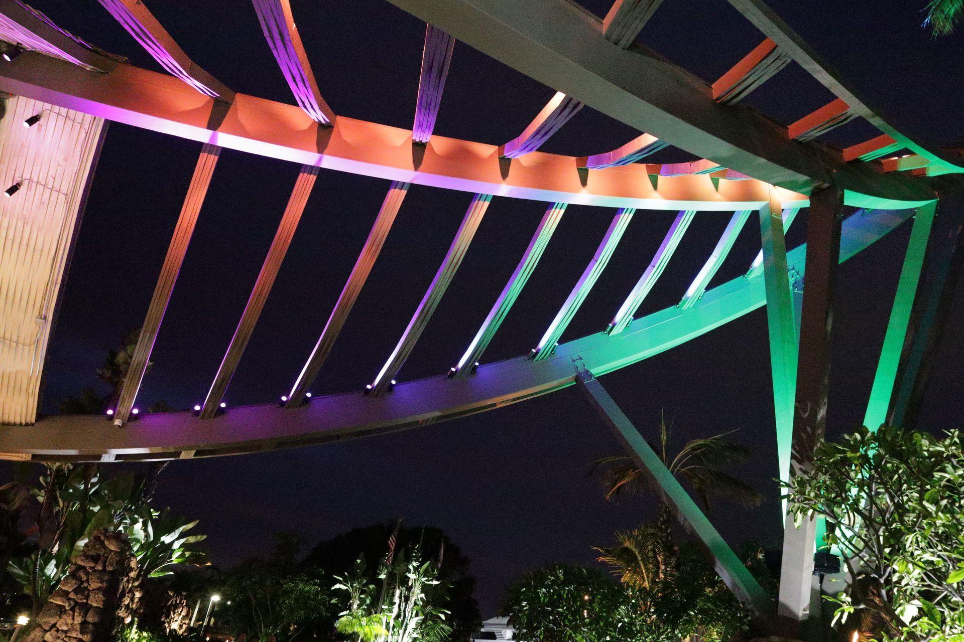 Colorfully lit bridge or overpass at night with purple, green, and pink lights against a dark sky