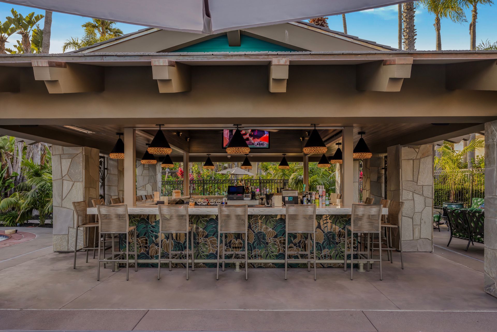 Open-air bar with teal roof, hanging lights, and bar stools in a tropical setting