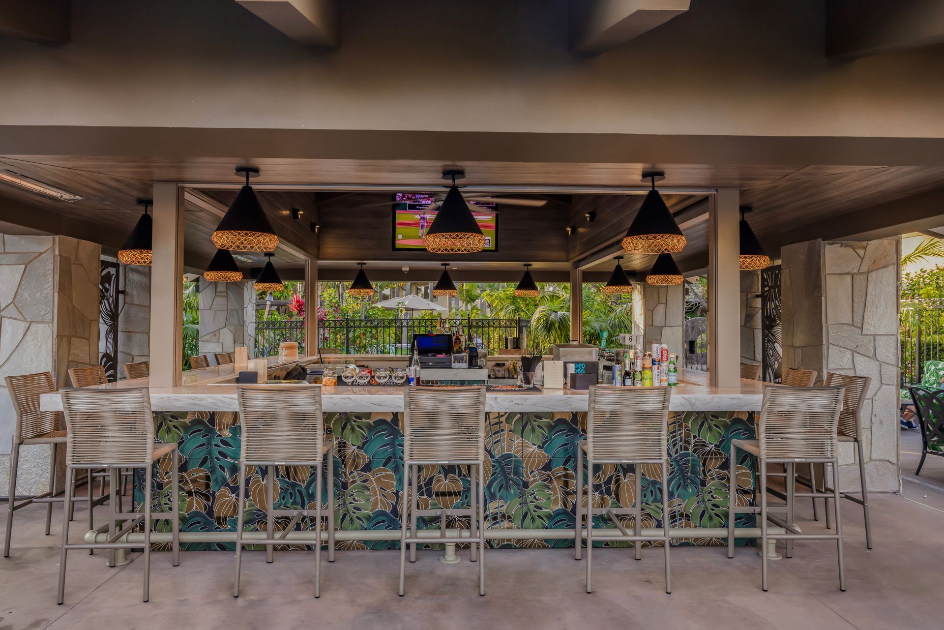 Open-air bar with patterned tile counter, hanging pendant lights, and bar stools in a tropical setting