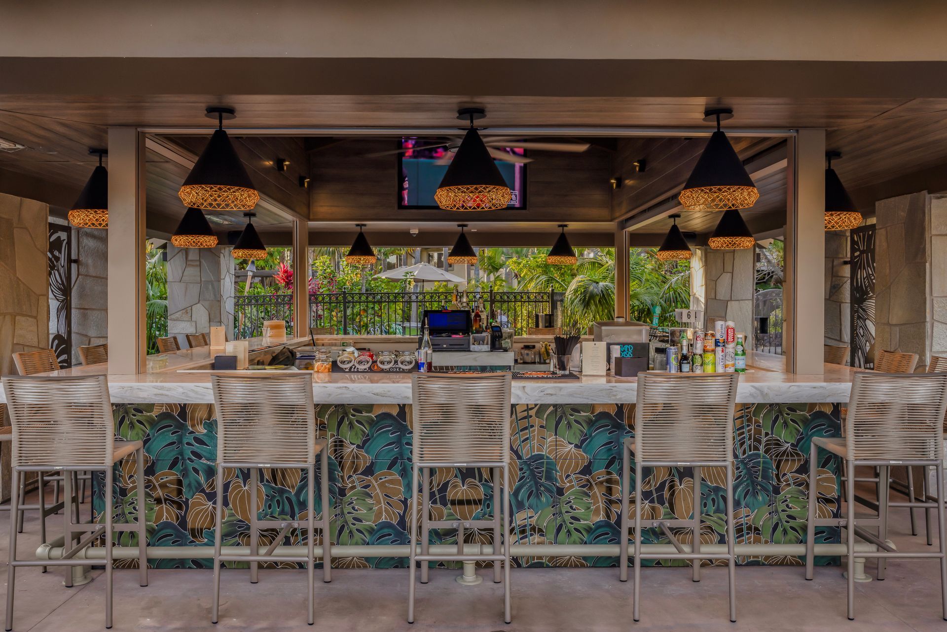 Open-air bar with woven stools, hanging lamps, and tropical decor at sunset