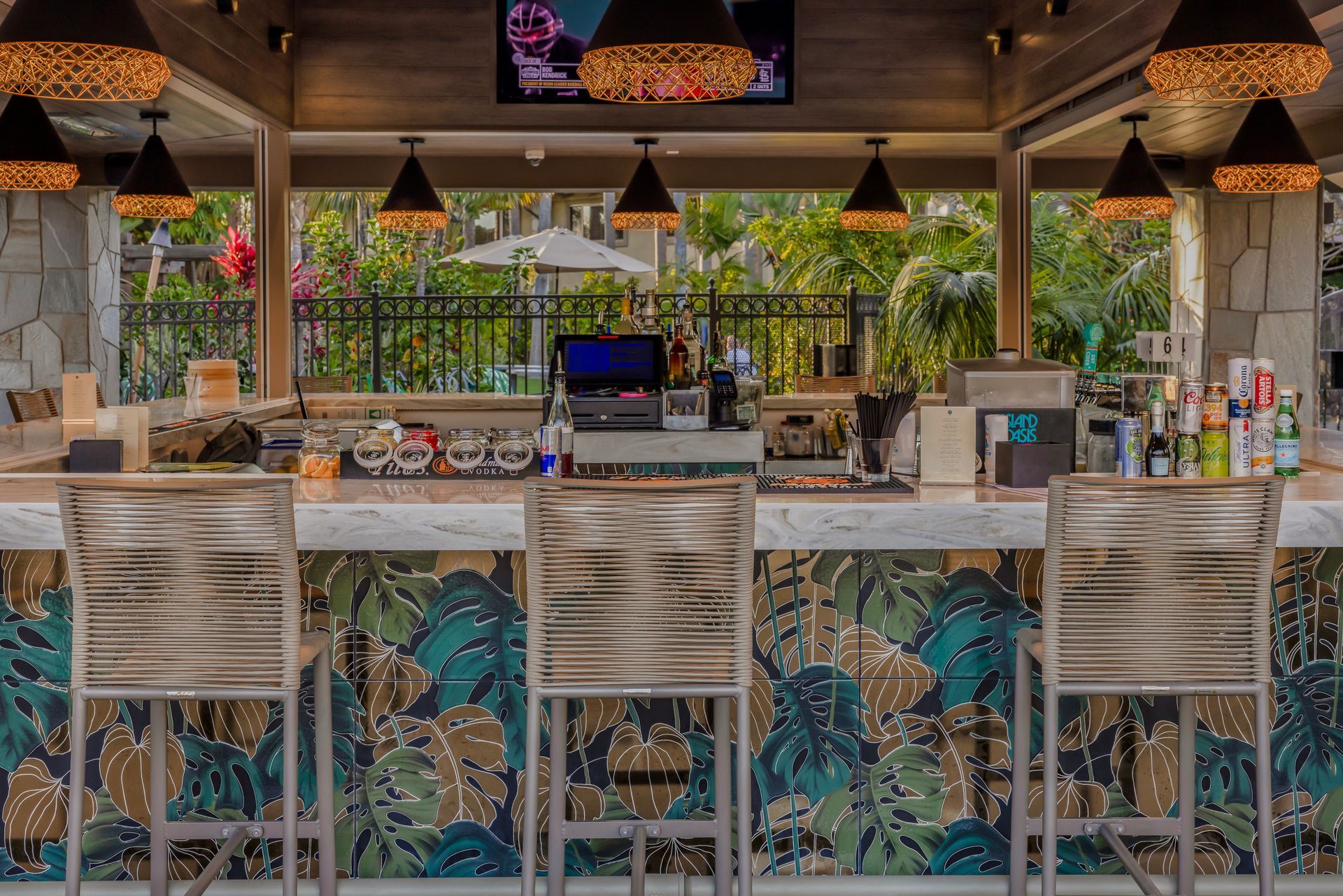 Empty tropical bar with patterned stools, hanging lights, and a bright outdoor view.