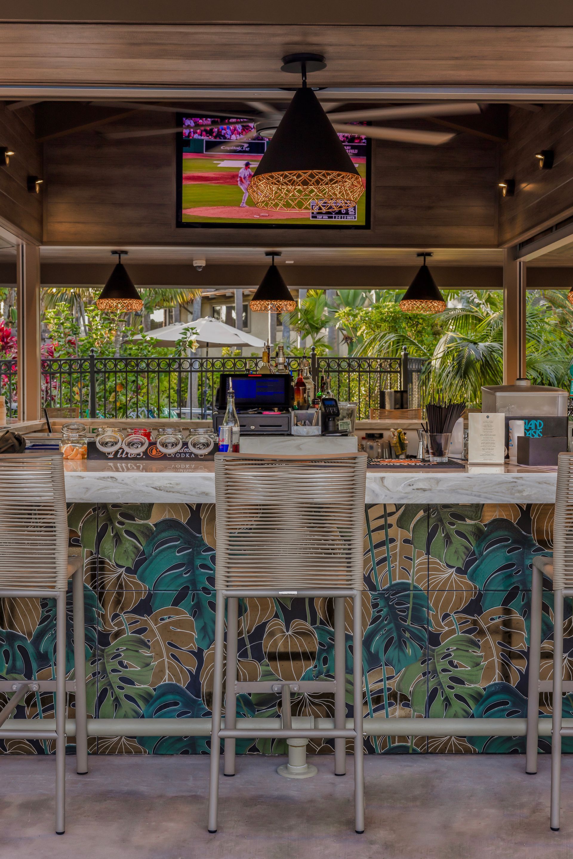 Open-air bar with patterned stools, hanging lamps, and a TV showing a sports game