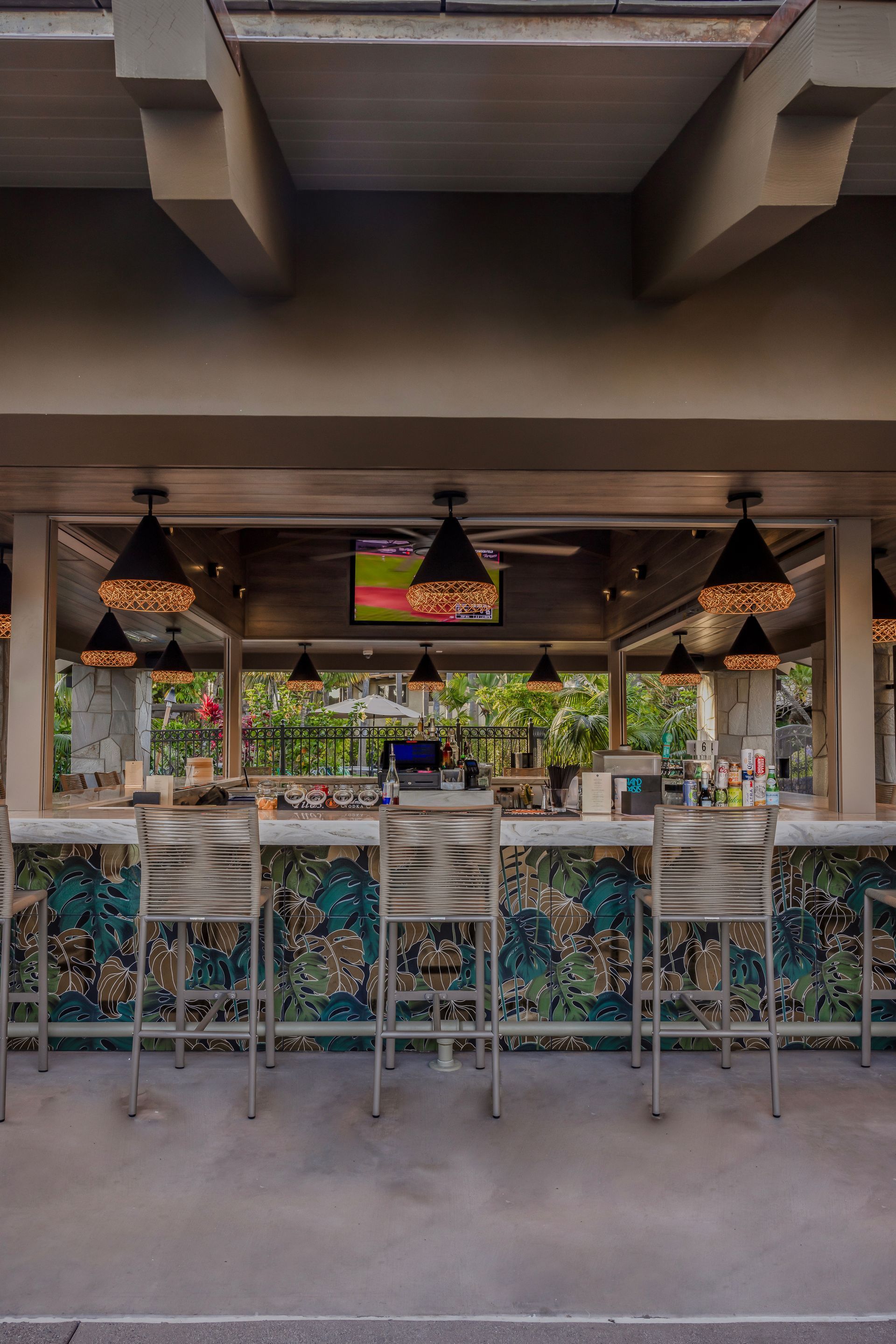 Outdoor café bar with hanging pendant lights, colorful decor, and rows of stools under a shaded patio