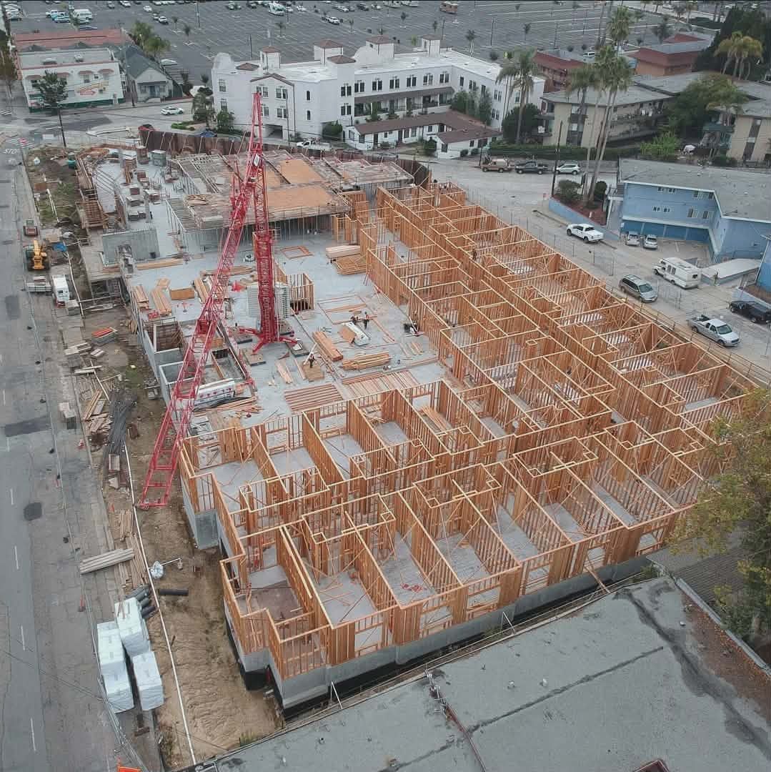 Aerial view of a construction site with orange wooden framing and a red crane near a street.