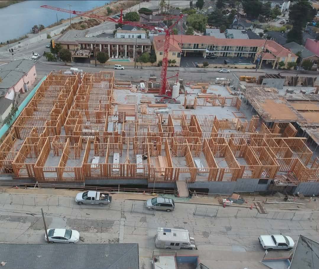Aerial view of a large construction site with steel framing and cranes near a waterfront road