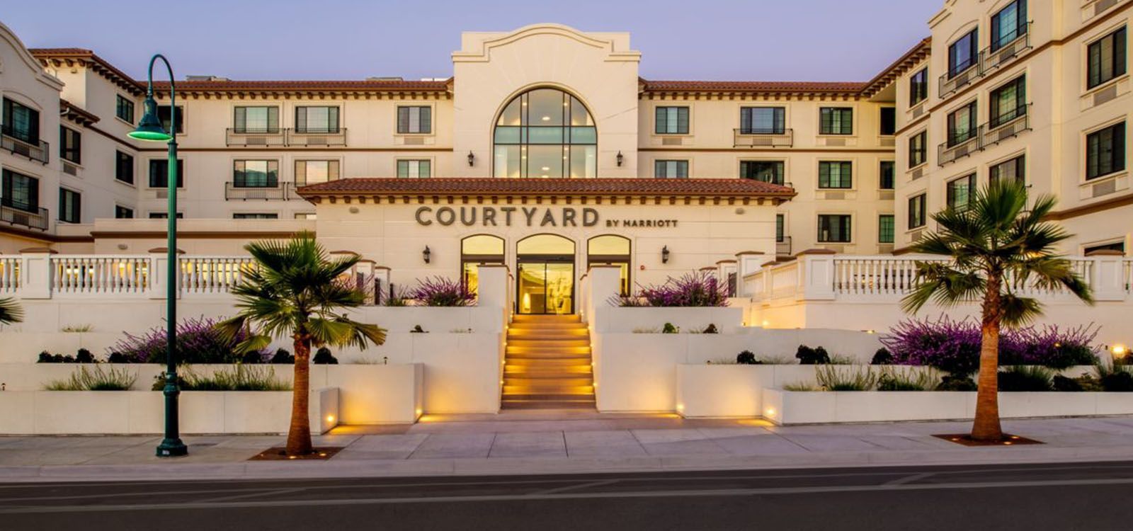 Courtyard hotel exterior at dusk with lit central staircase and palm trees