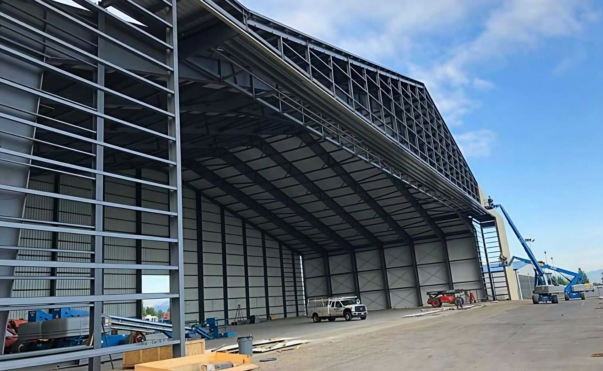 Large industrial building under construction with steel framing, open entrance, and blue sky overhead