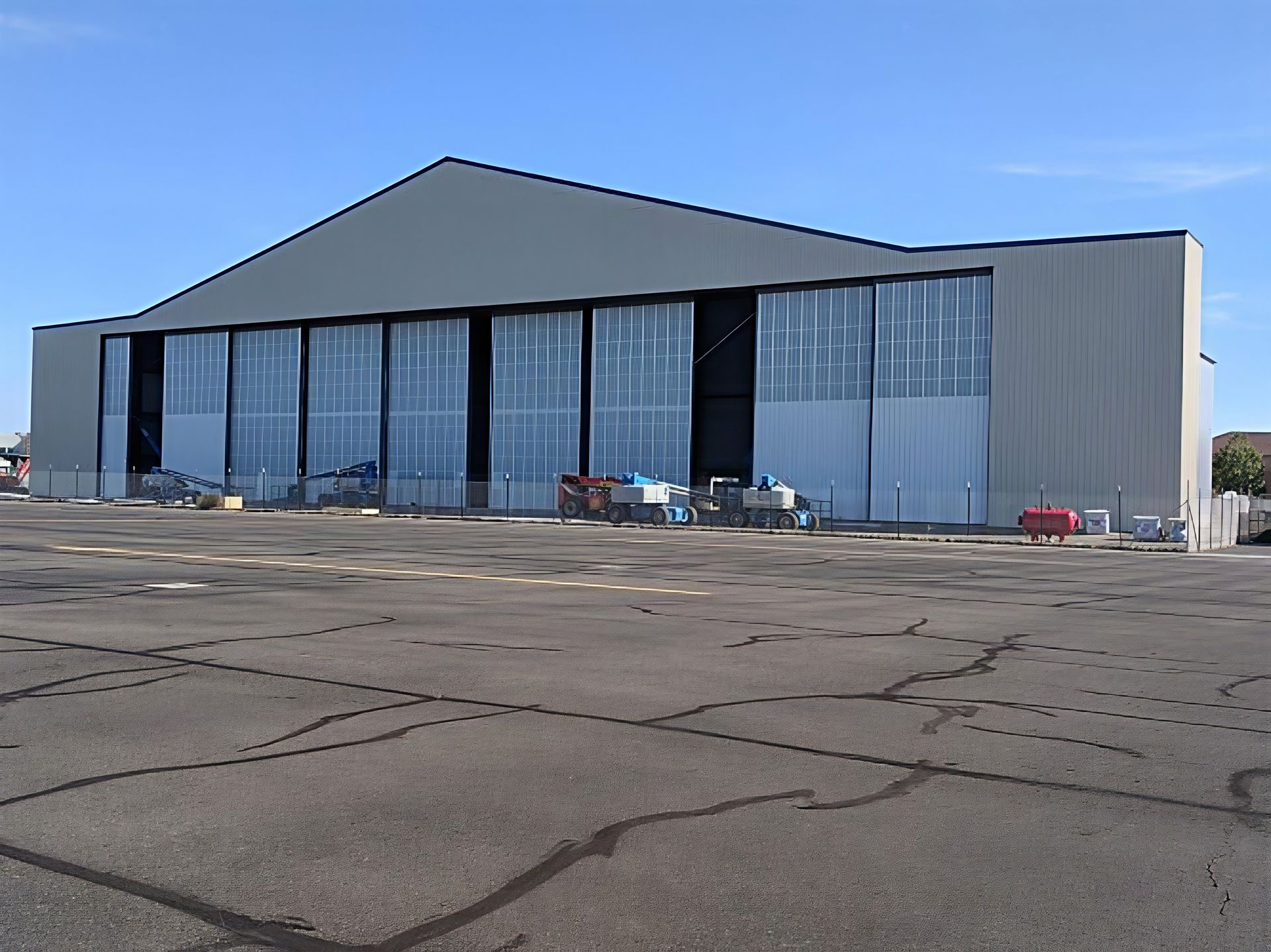 Large industrial building with blue-tinted glass panels and a gray roof on a cracked paved lot under a clear sky