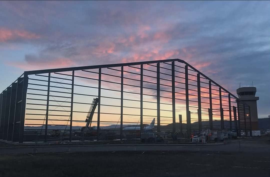 Glass building at sunset with cranes silhouetted against a pink and orange sky