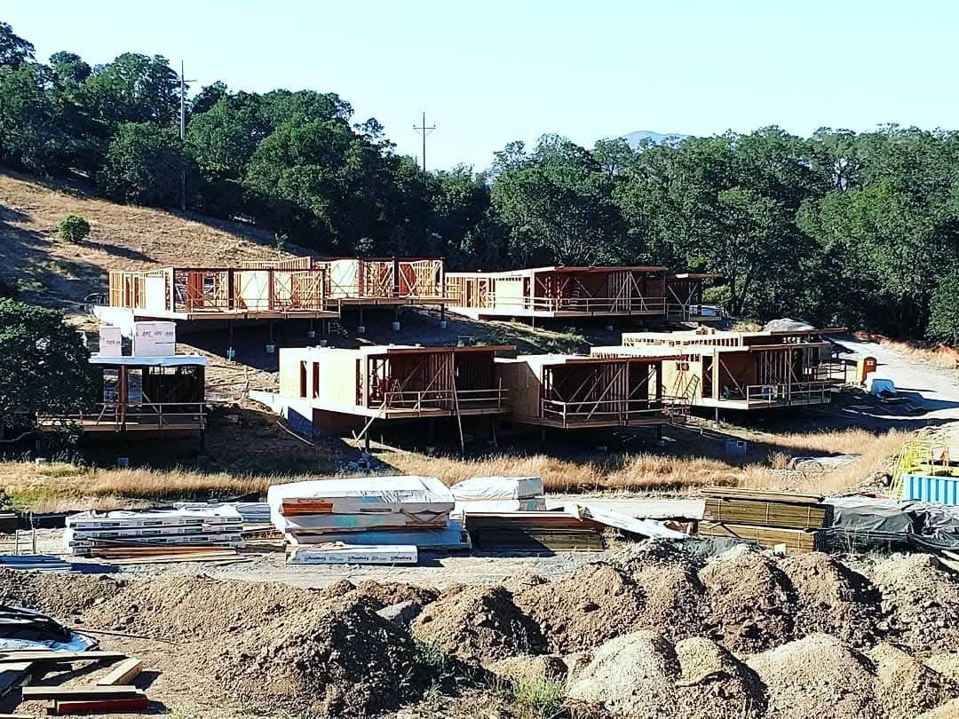 Partially built homes on a hillside construction site with dirt piles and trees in the background