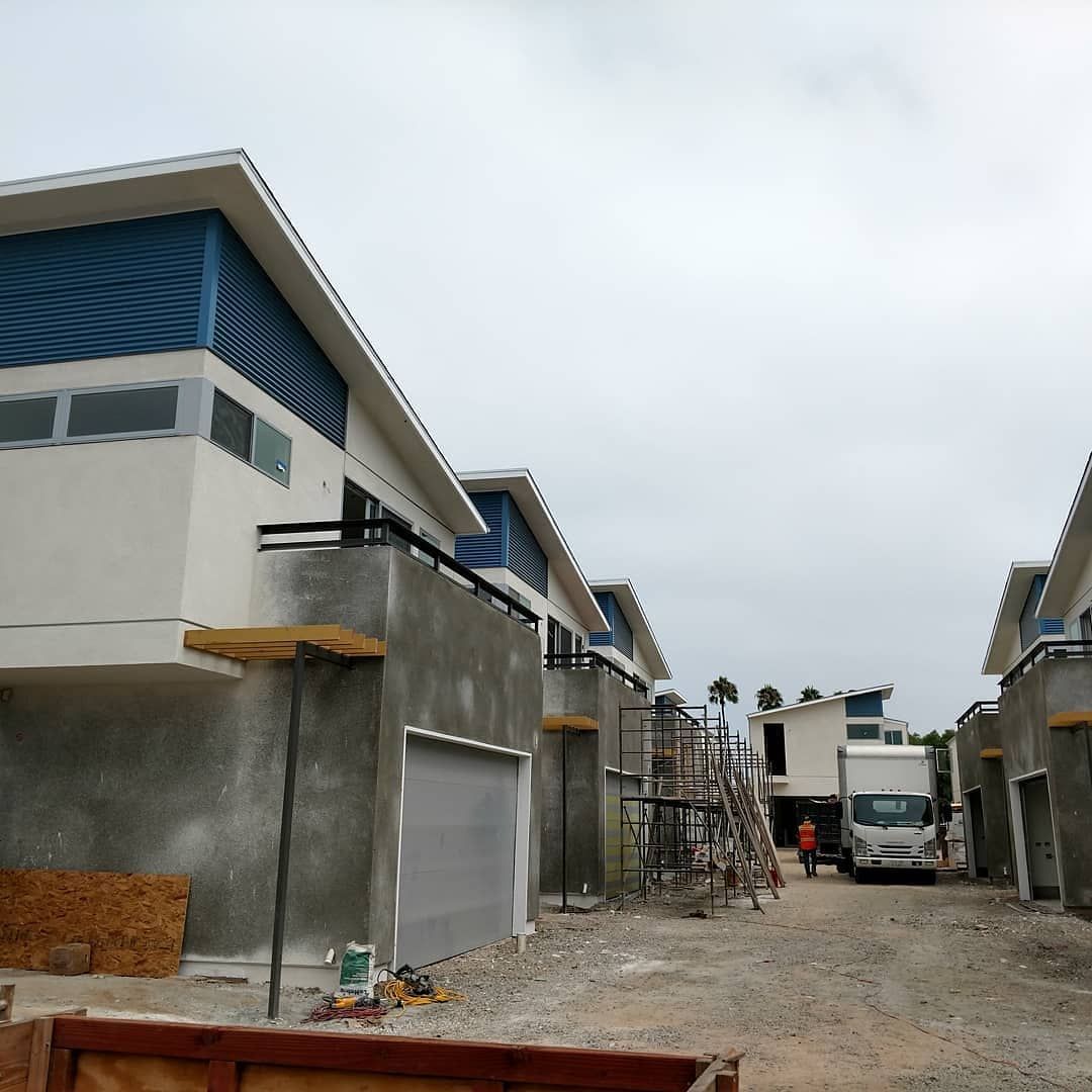Residential construction site with unfinished row houses, scaffolding, and a dirt road between buildings