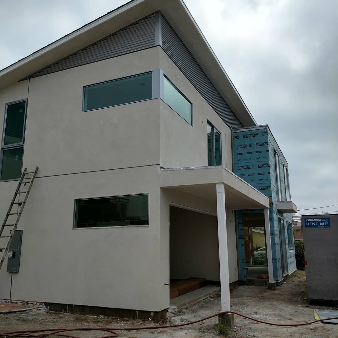 Modern white two-story building with large windows and a covered entrance under a cloudy sky
