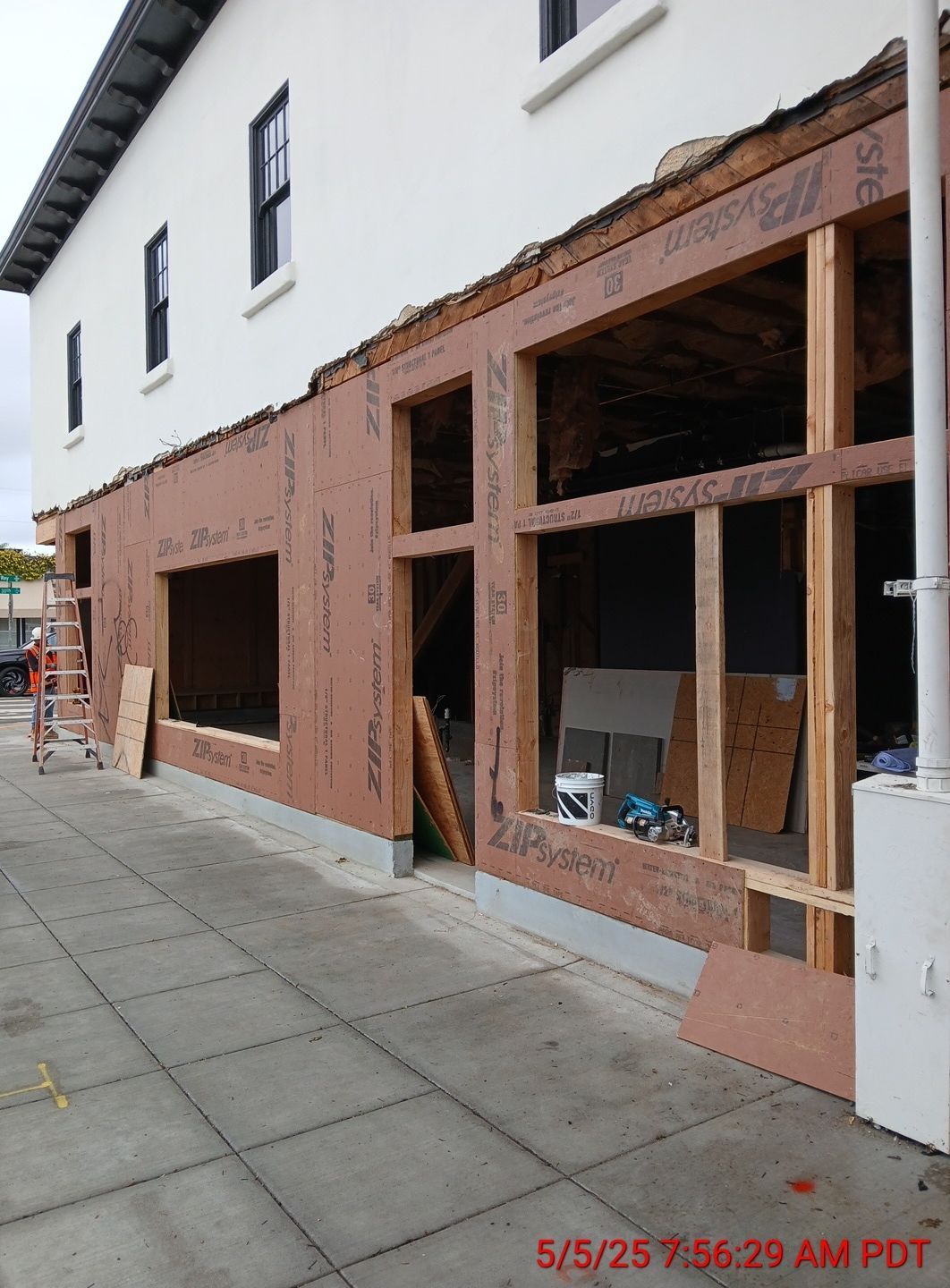 Street-level storefront under construction with exposed wood framing and brown sheathing on a white building