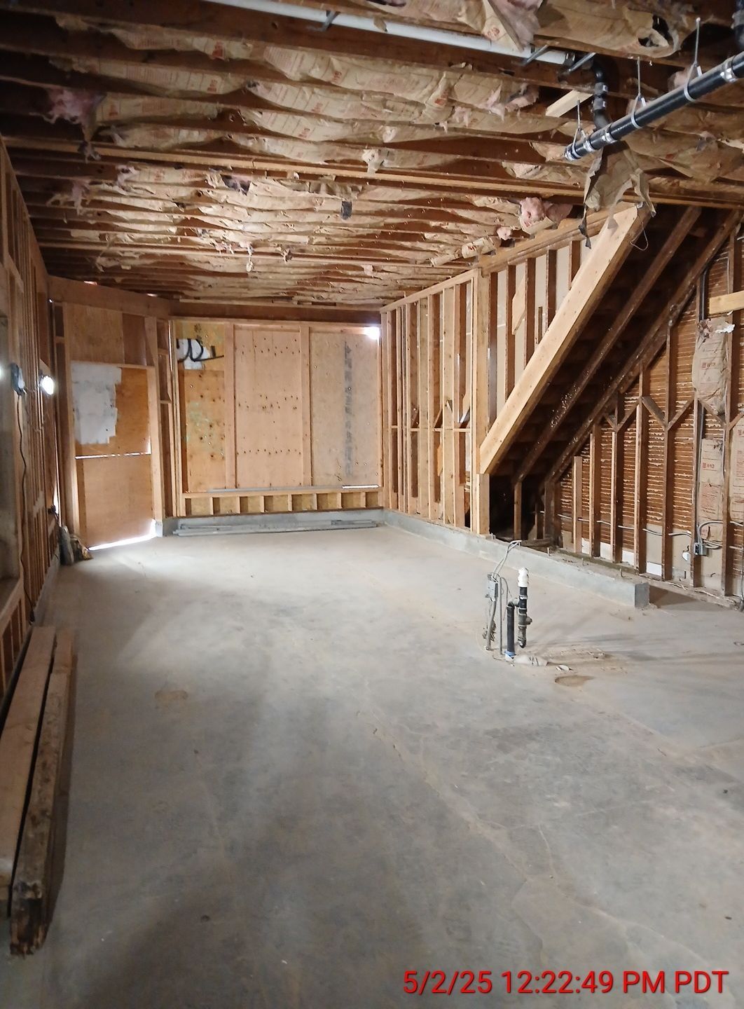 Unfinished basement interior with exposed studs, stairs, concrete floor, and insulation in the ceiling.