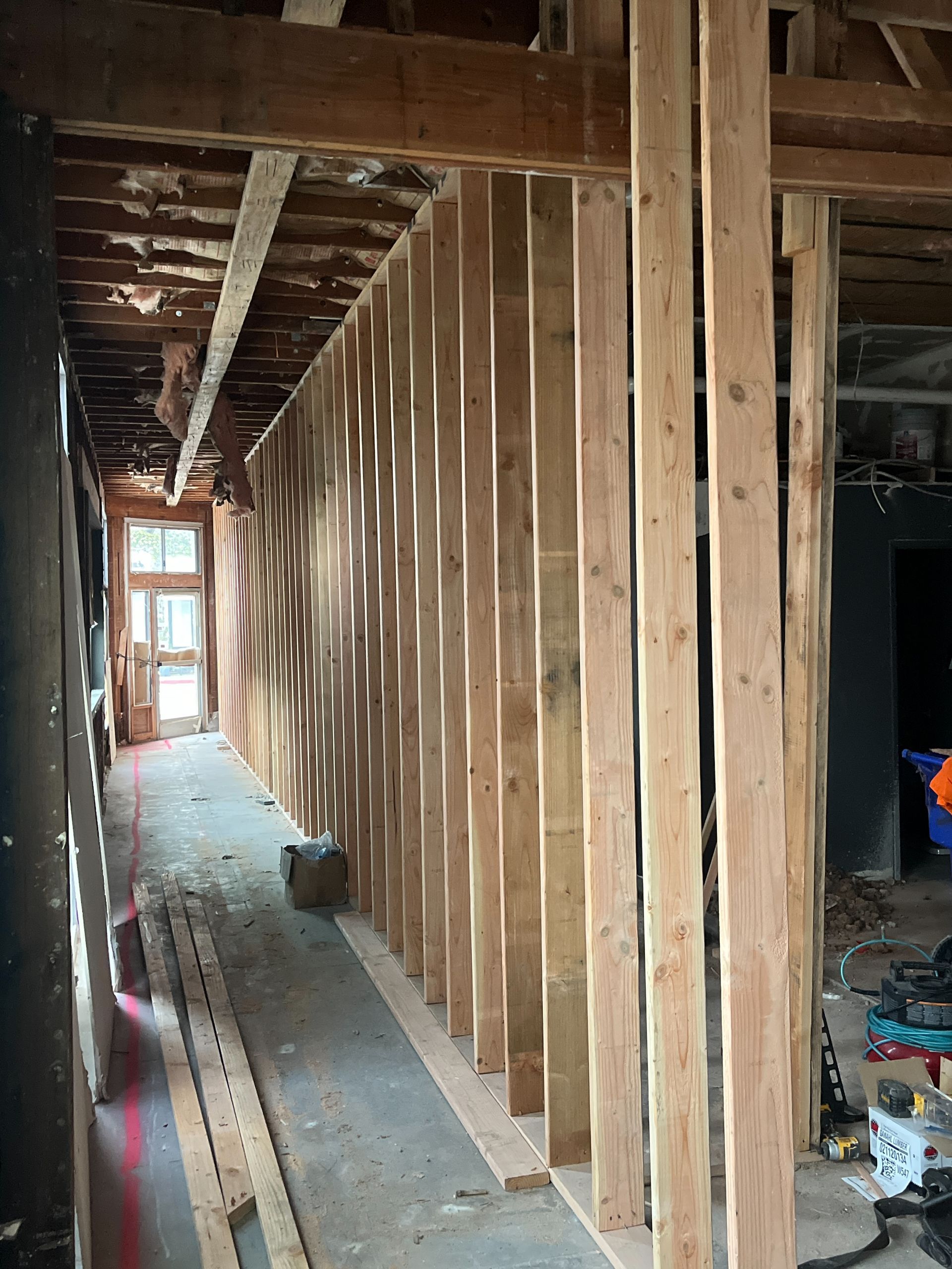 Partially finished hallway with exposed studs and ceiling beams, leading to a bright window at the end.