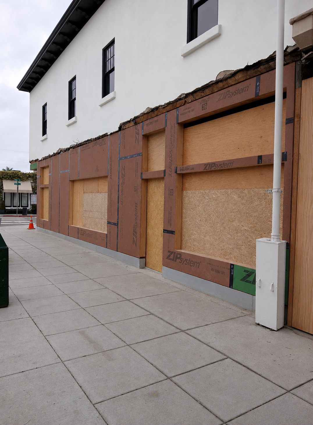 Boarded-up building facade with brown plywood panels and boarded windows along a sidewalk.