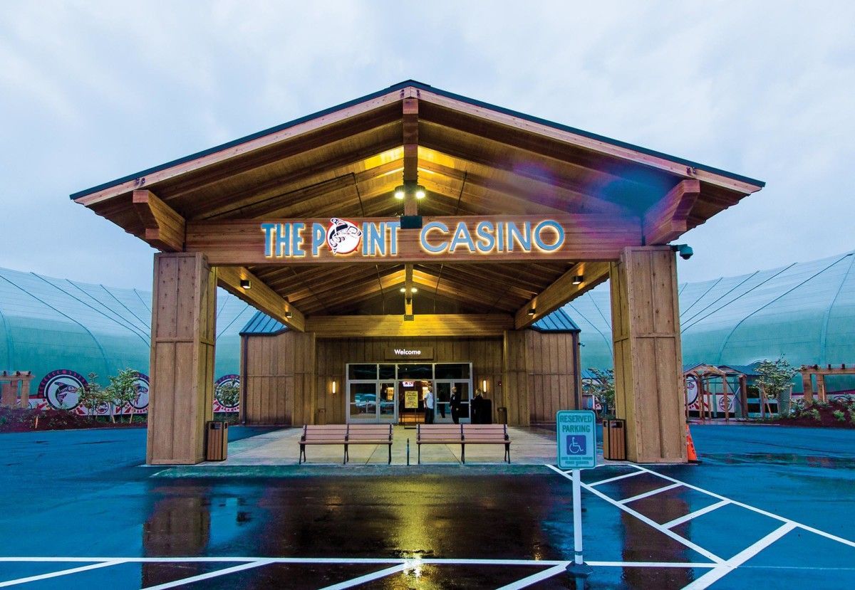 Entrance to The Point Casino, a wood-paneled building with neon sign on a wet parking lot at dusk