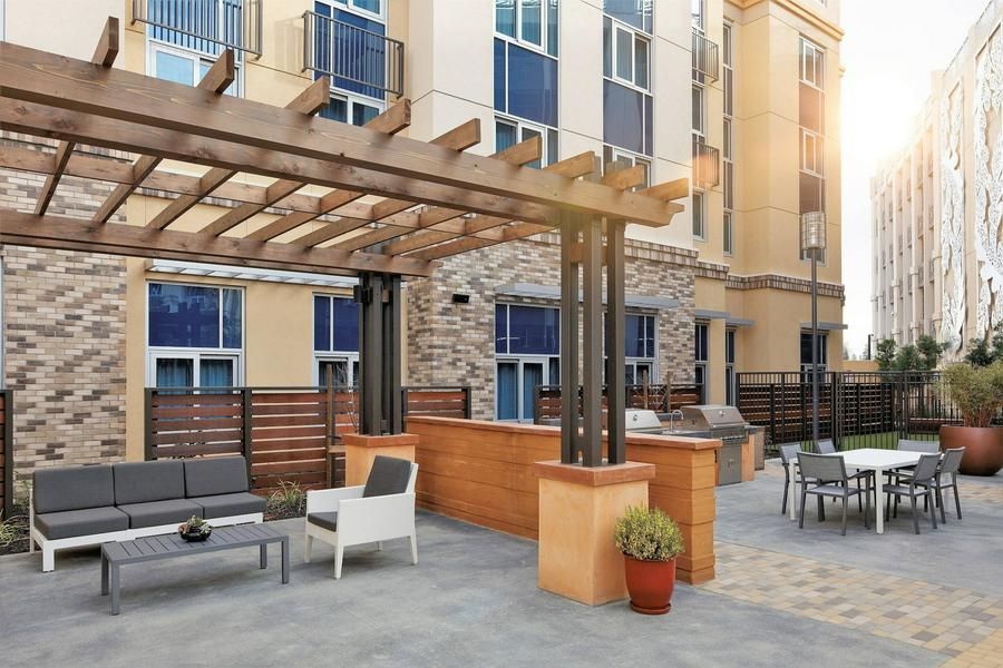 Modern apartment courtyard with pergola, gray seating, and outdoor dining tables in sunlight