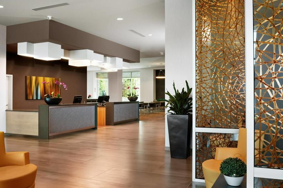 Modern hotel lobby with wood floors, reception desk, potted plants, and decorative wall panels