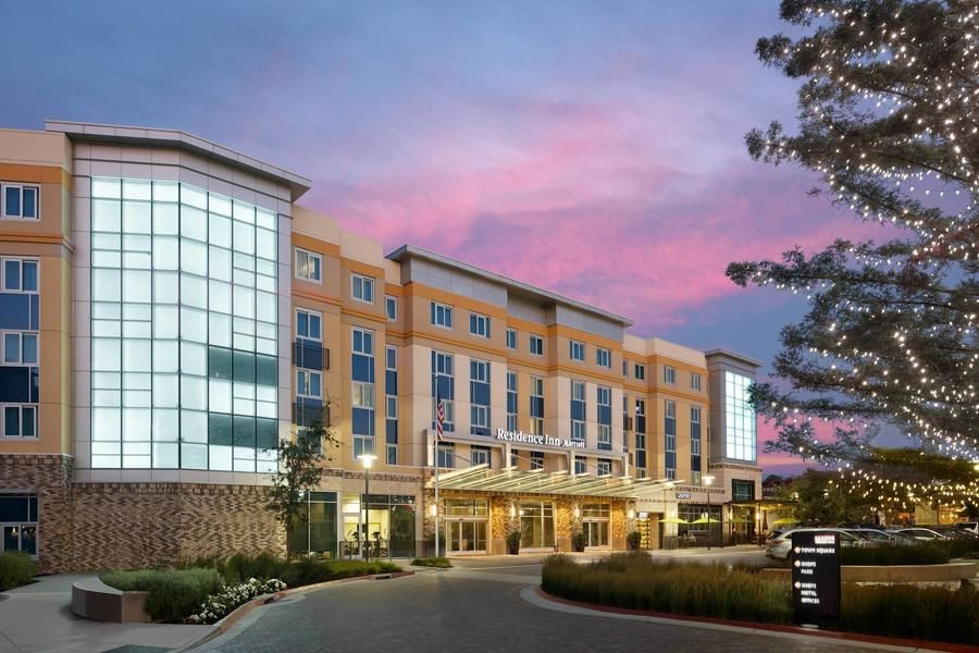 Modern hotel exterior at dusk with glass atrium, lit entrance, and pink sunset sky