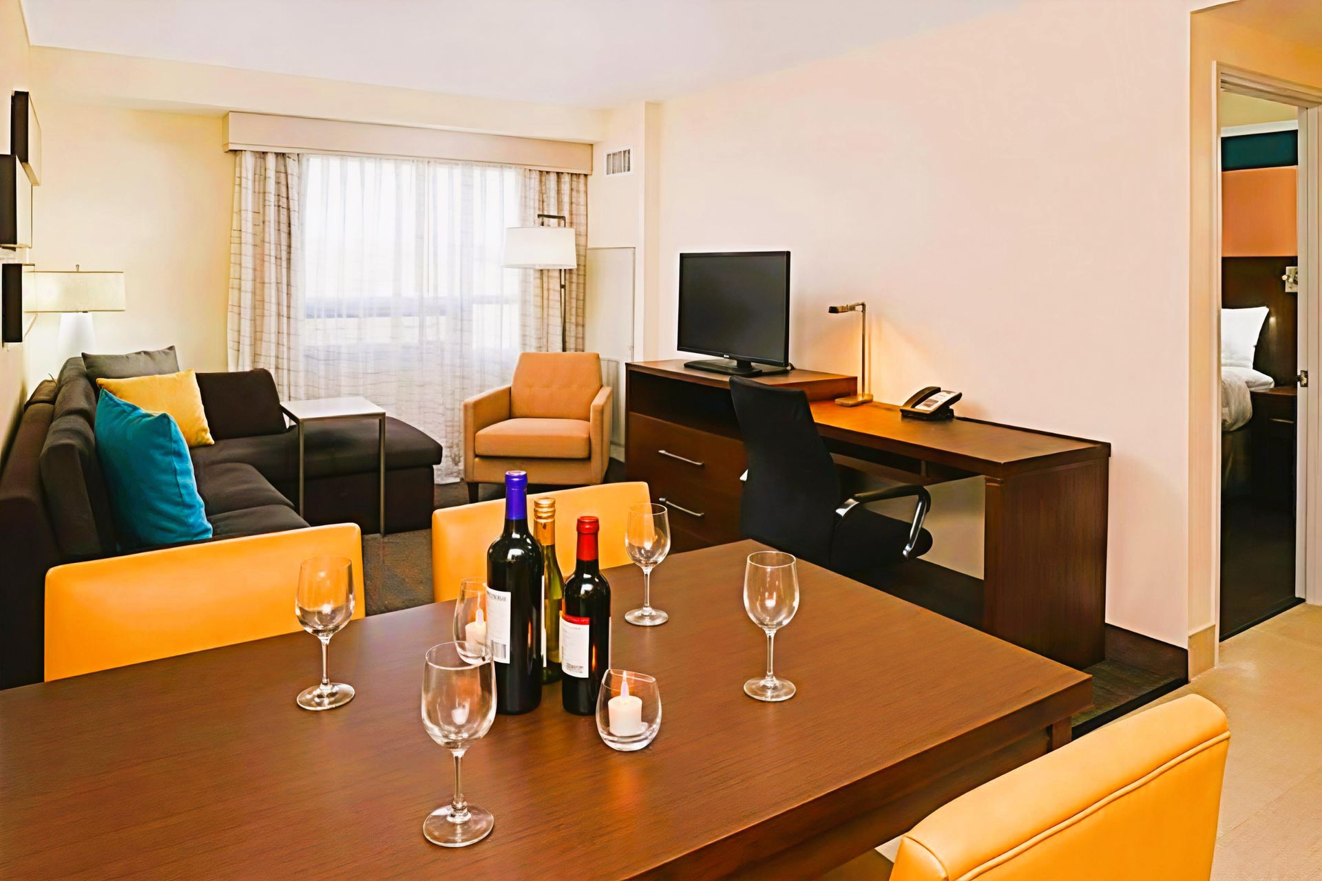 Modern living room with dining table, wine glasses, sofa, armchair, TV, and large window with curtains