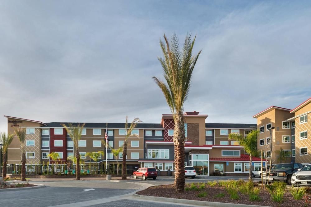 Modern apartment building with storefronts and palm trees in a parking lot at dusk