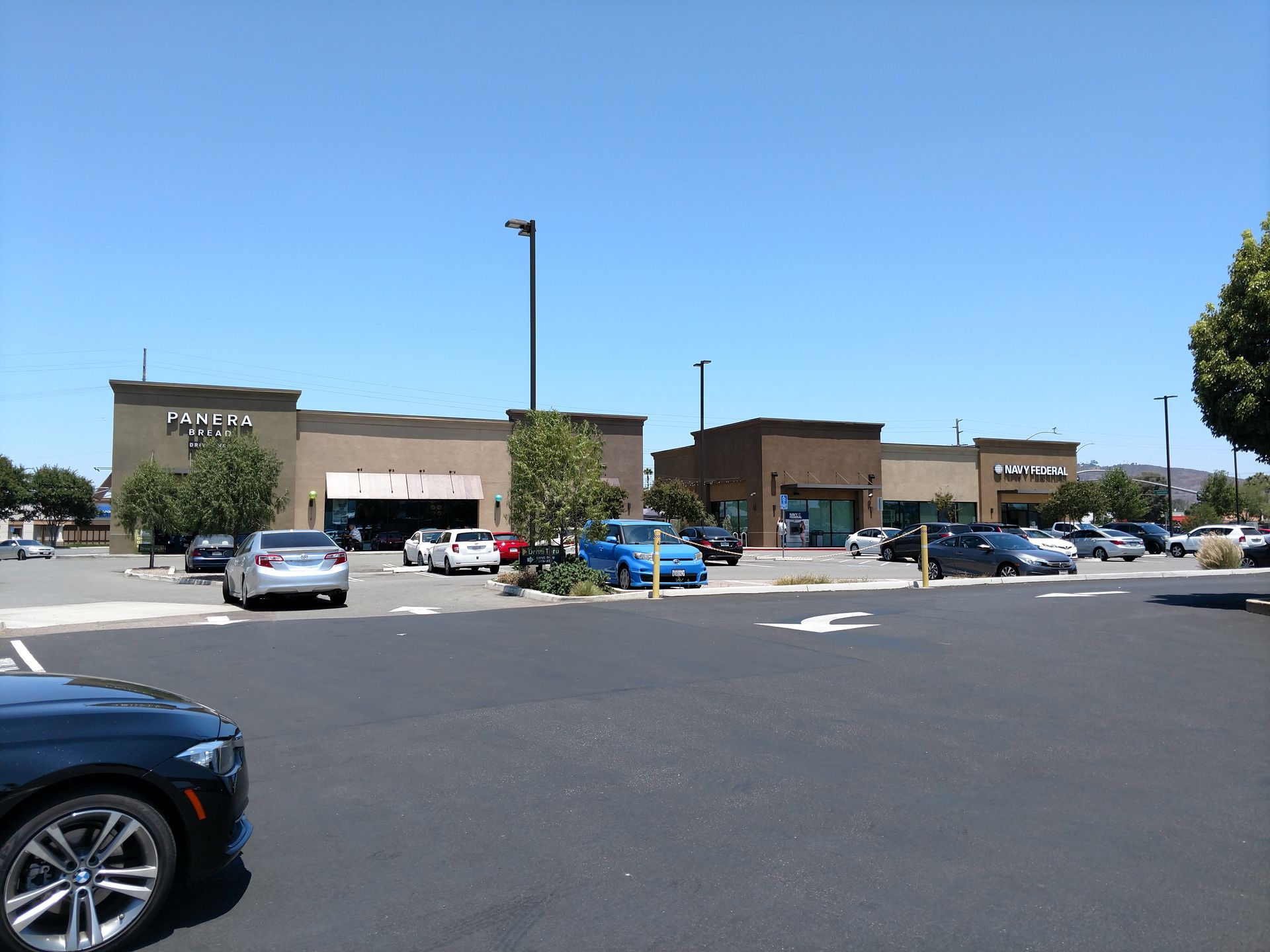 Shopping center parking lot with several parked cars under a clear blue sky