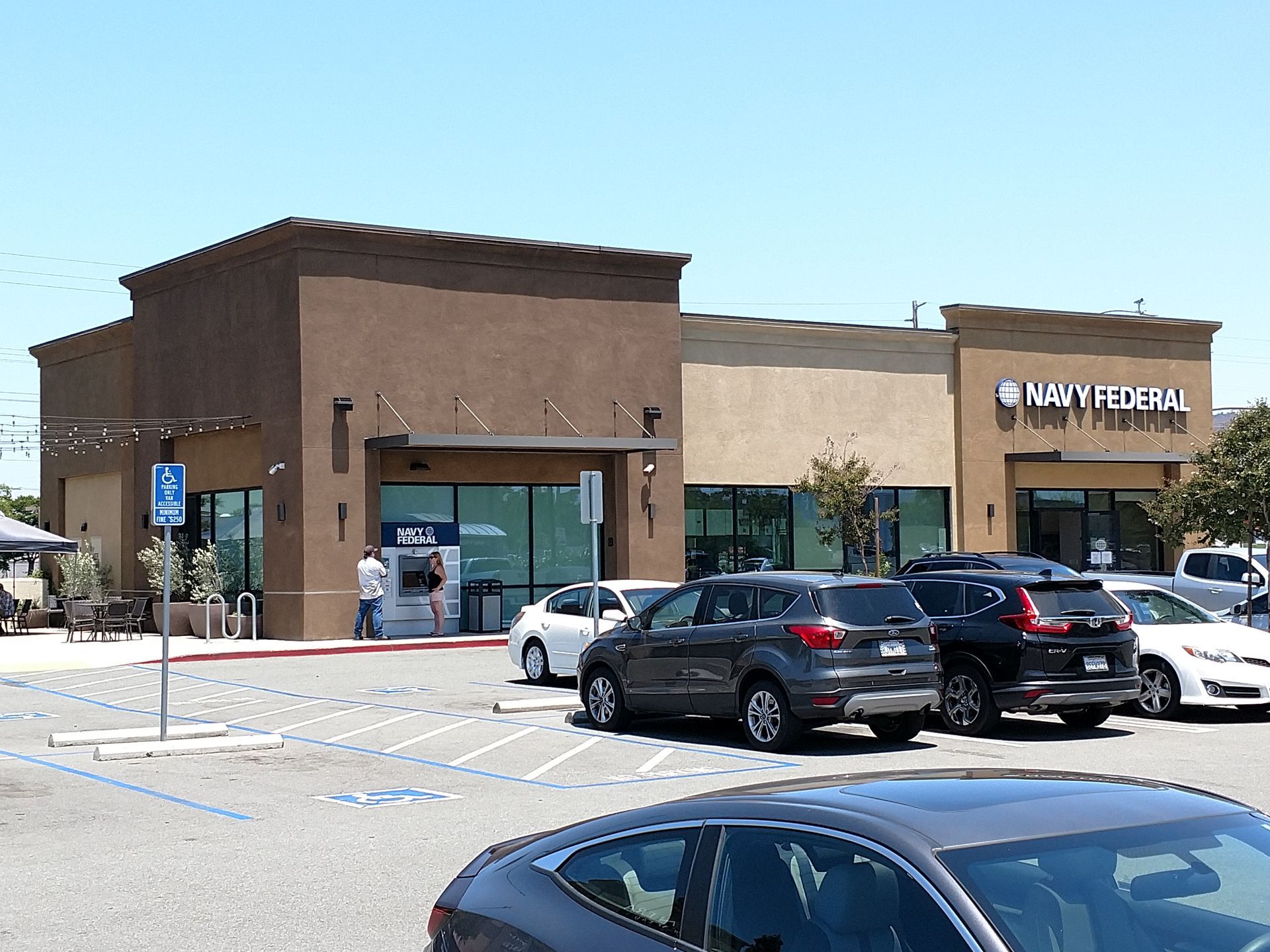 Shopping center storefront with parked cars in front on a sunny day