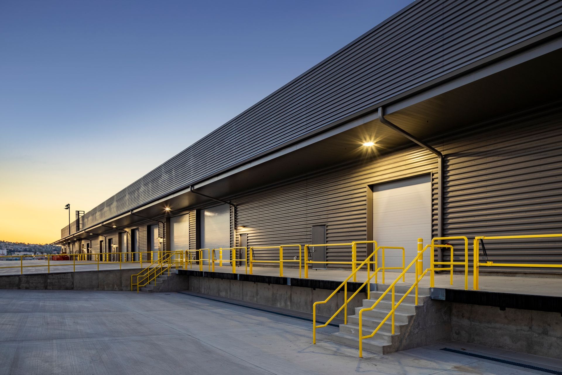 Industrial warehouse loading dock at dusk with yellow railings and closed bay doors